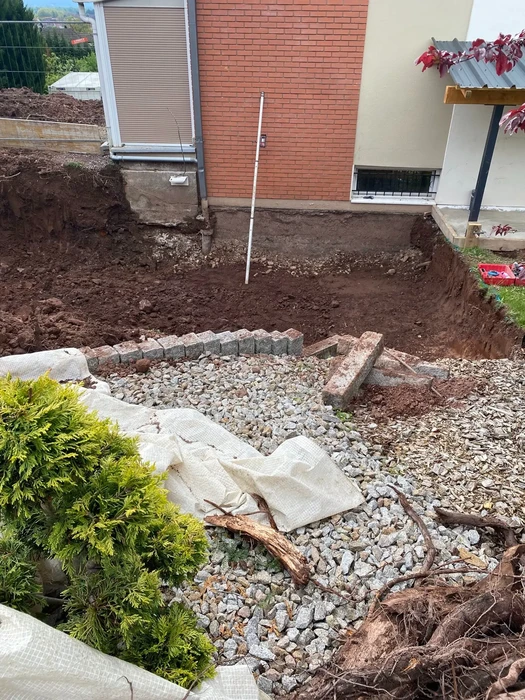 Chantier d'aménagement extérieur résidentiel avec excavation de terrain autour d'une maison moderne en briques