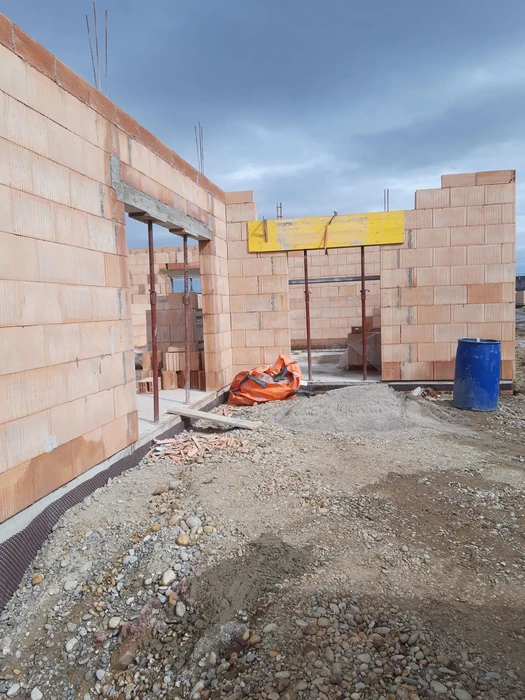 Chantier de construction résidentielle en cours avec ouvriers en équipement de sécurité orange travaillant sur structure en blocs de béton cellulaire