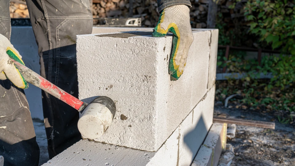 Un maçon en tenue de travail pose des blocs de béton cellulaire sur un chantier extérieur