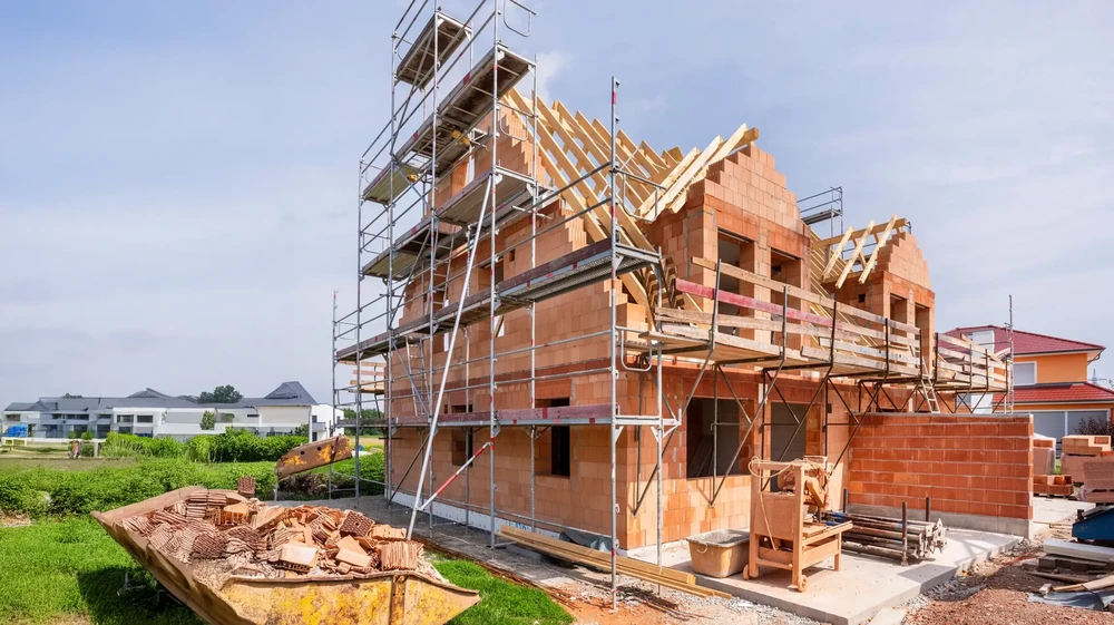 Chantier de construction résidentielle en cours, maison individuelle à étages avec murs en briques rouges et charpente bois apparente