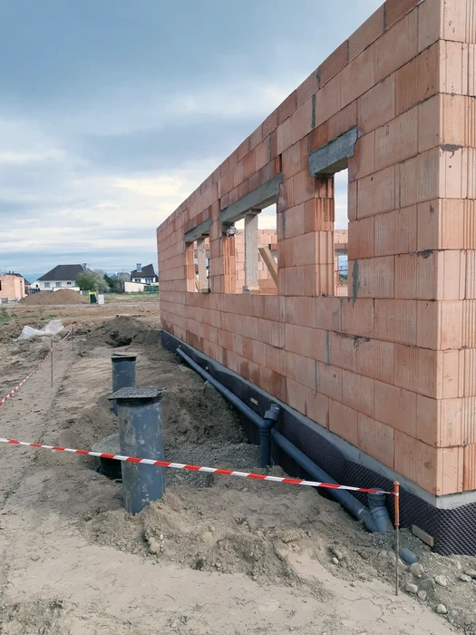 Chantier de construction résidentiel en cours, mur en briques de terre cuite avec ouvertures pour fenêtres, terrain excavé avec barrière de sécurité rouge et blanche