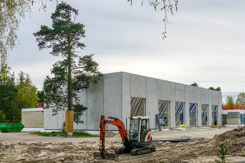 Chantier de construction extérieur avec homme en tenue de travail, casque de sécurité jaune, bras croisés devant bâtiments en construction